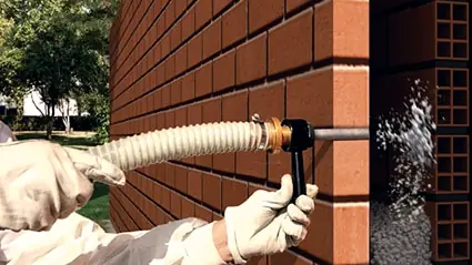 Corte de una fachada de ladrillo con cámara de aire rellenándose de aislante